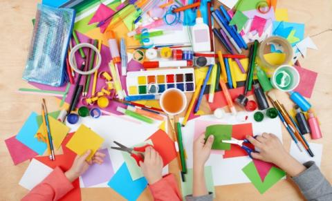 the arms of two children interacting with a table full of craft supplies