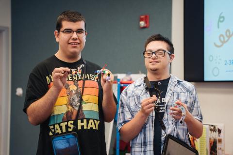 Photo of 2 adults with ASD smiling and holding a craft